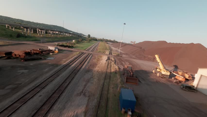 FPV drone weaves low over CN ore dock as taconite pellets load onto lake freighter along railroad tracks in Duluth Minnesota at sunset