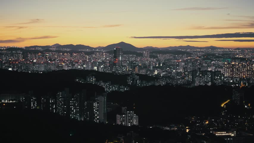 Wide panoramic view of Seoul city skyline at dusk with illuminated buildings, mountains and evening sky, South Korea.