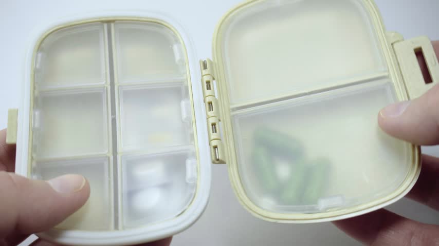 Close up of hands opening a pill organizer and showing tablets inside. Medication storage container for organizing daily medicines and supplements at home