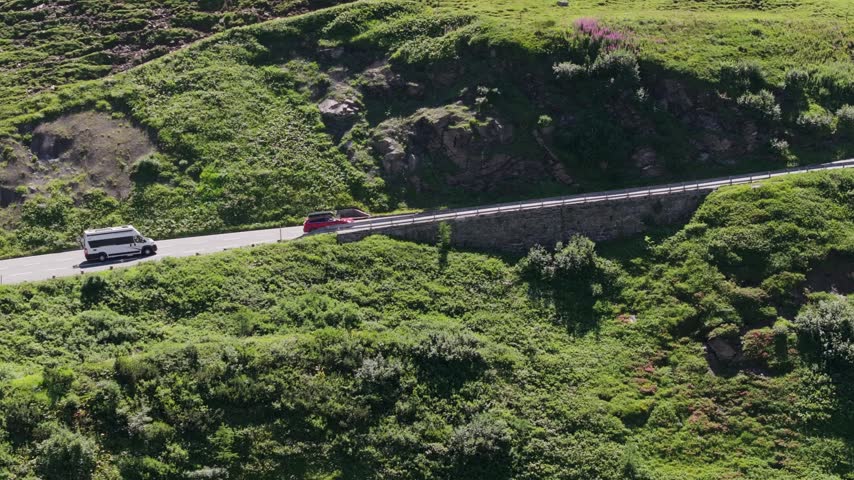 Cars and camper travel sweeping alpine bends amid lush slopes in Austrian Alps