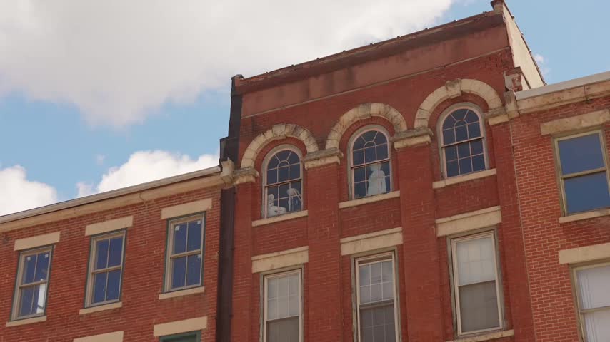 Historic red brick building facade with arched upper windows and mannequins inside on a bright daytime sky.