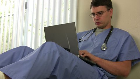 Doctor with Laptop takes a call VIDEO (Doctor sitting and working on a laptop takes a cell phone call and rushes off 