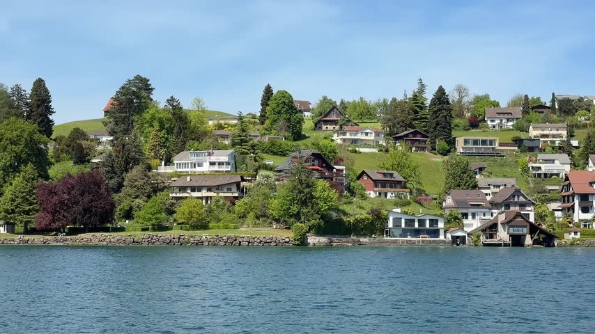 Scenic footage of Lucerne, Switzerland, presents the town from its riverside setting, with houses and buildings creating a distinctive waterfront urban landscape. The combination of Swiss architecture, residential surroundings, and river scenery provides versatile material for travel documentaries, tourism promotions, vacation guides, European destination stories, city features, and Switzerland-focused productions.
