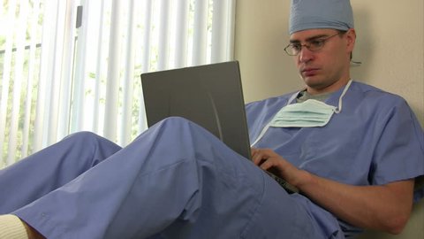 Surgeon sitting and working on a laptop takes a cell phone call and rushes off