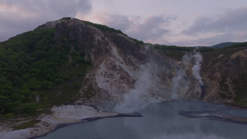 Gas and steam rise from geothermal pond on mountaintop at sunset