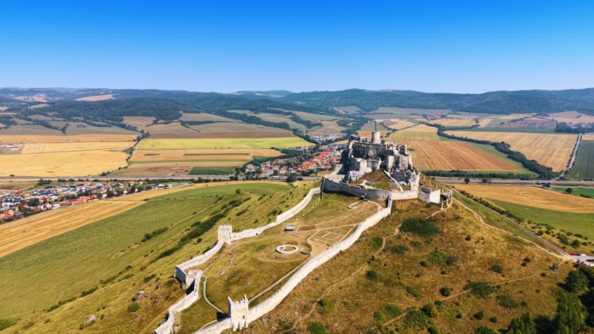 Hilltop castle near town. A view of a castle on a high hill in Slovakia with green fields and a small town nearby on a clear day.