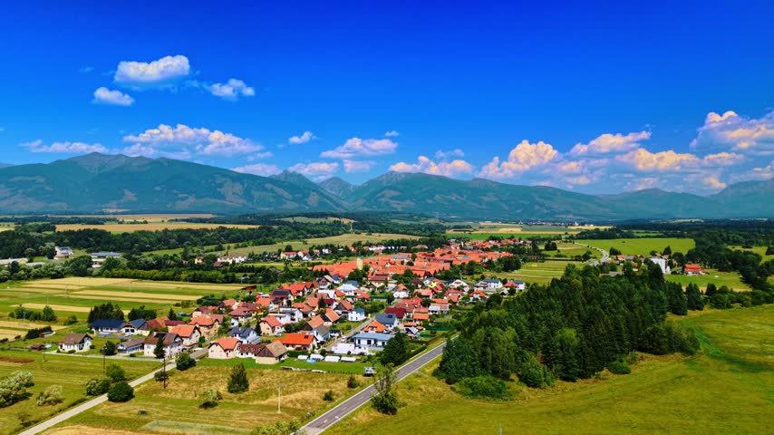 Aerial view of a valley village near alpine ridge, Slovakia. High angle landscape of a countryside town, asphalt road, pine forest, and mountain peaks in Liptov region.