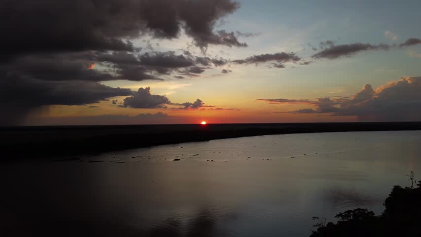 Drone view of a spectacular sunset over a large river in the Orinoco Delta, featuring clouds and reflections