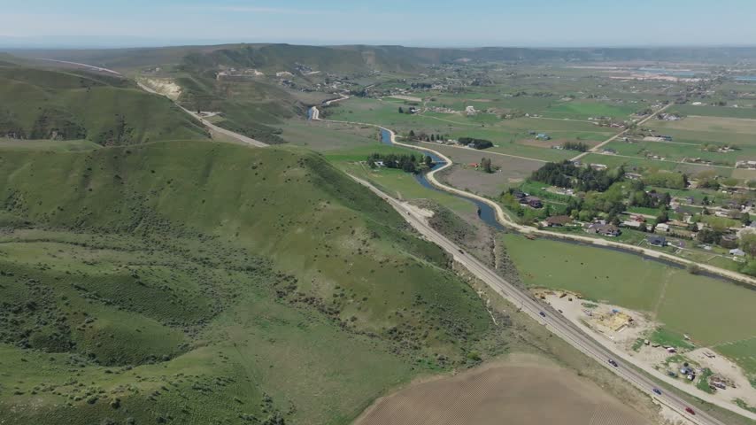 Aerial view of the rolling green hills and winding canal near Emmett, Idaho, with rural farmland and a road stretching through the landscape in Emmett, Idaho, United States.