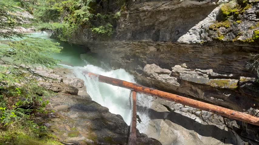 Johnston Creek river in Johnston Canyon in the Banff National Park. British Columbia, Canada. River water flows rapidly over rocks under a wooden bridge surrounded by trees in a natural setting