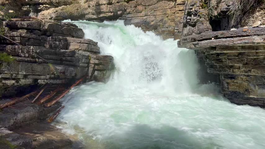 Johnston Creek river in Johnston Canyon in the Banff National Park. British Columbia, Canada. Water flows rapidly over rocks in a gorge, creating foam and splashes with greenery visible in the background
