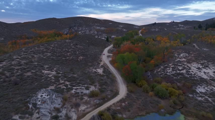 Aerial view of a winding dirt road through the rocky landscape of Castle Rocks with vibrant autumn foliage at dusk in Castle Rocks, Idaho, United States.