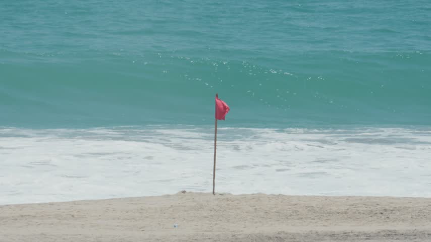 Red flag on a beach signaling danger as powerful ocean waves crash on the shore of puerto escondido