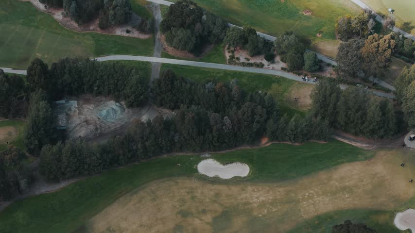 Top-down view of a lush green golf course with bunkers, trees, and fairways
