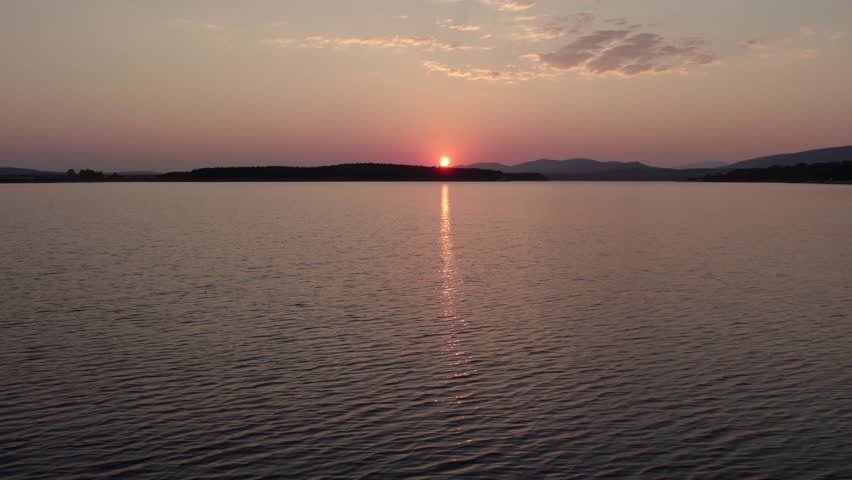 Scenic aerial view of the sun setting behind mountains during a total solar eclipse, with its light reflecting on the Cuerda del Pozo lake