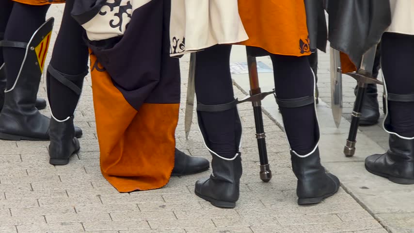 Mid section slow motion shot of participants wearing detailed medieval knight costumes with leather belts, bracers and embroidered tunics during Moros y Cristianos festival parade, horizontal 4K.