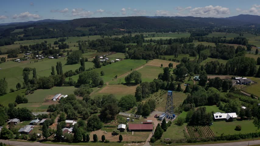 Panoramic aerial view of countryside fields, homes and a utility tower