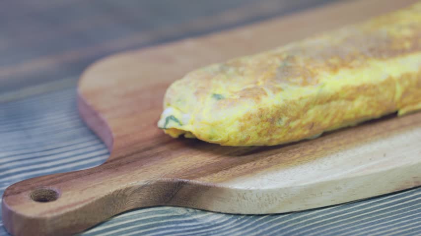 A close-up shot of a chef slicing freshly cooked Korean rolled omelette (Gyeran-mari) with a knife on a wooden cutting board. 