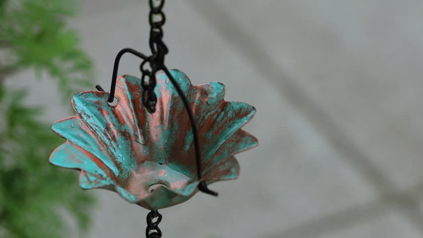 Rain Chain Part 2. A slow-motion close-up shot of a raindrop dripping into a vintage copper rain chain cup with turquoise patina. Soft blurred background on a rainy day.
