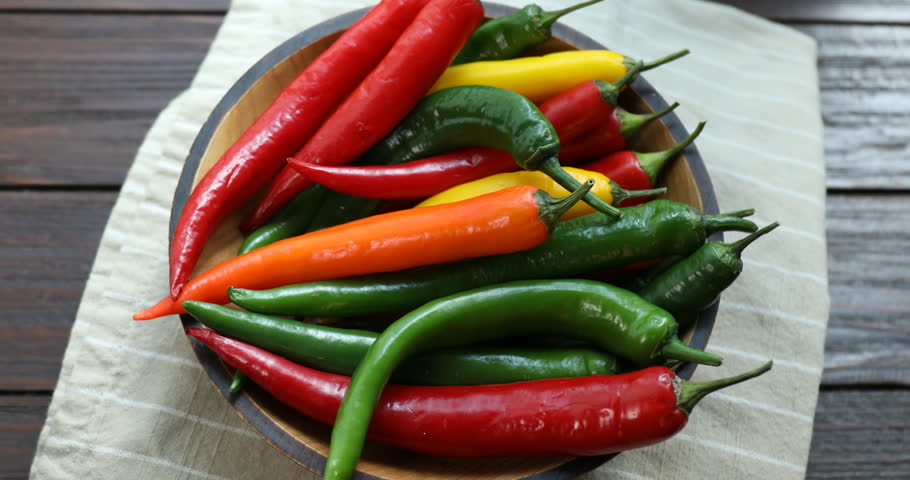 Colorful chili peppers in bowl on table, rotating