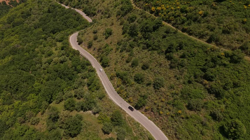 Aerial view of a winding road through lush green hills with cars driving along the mountain pass in Muzine, Qarku i Vlores, Albania.