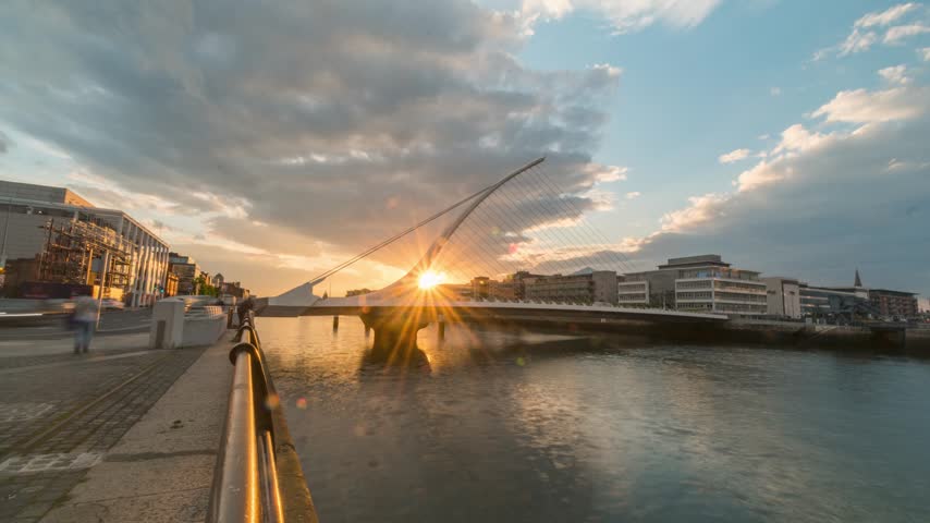 Day-to-night timelapse of the Samuel Beckett Bridge over the River Liffey, sun setting behind its harp-shaped mast.
