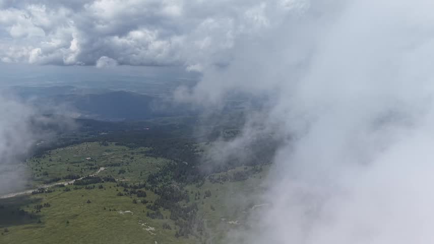 A green mountain landscape with forest and open slopes is temporarily obscured by dense drifting clouds before the valley becomes visible again.