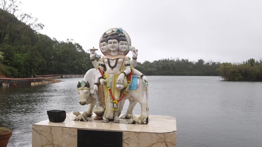 Wide view of a large, intricate Hindu deity statue resting peacefully beside the sacred crater lake at Ganga Talao Grand Basin