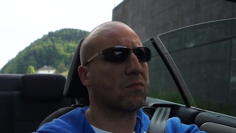 male is driving a convertible car in a landscape with mountains