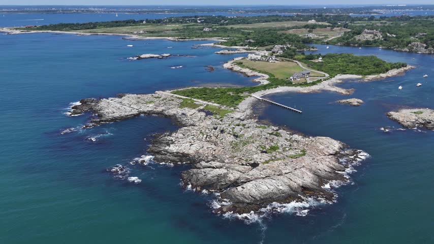 Wide aerial view revealing a dramatic jagged rocky peninsula jutting into the ocean, featuring exclusive waterfront estates along the iconic coastline of Newport, Rhode Island.