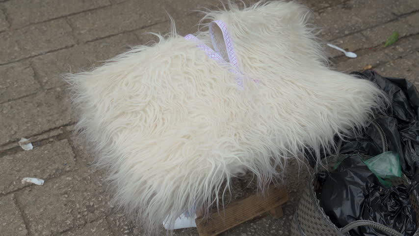 Static close up shot of a handmade white sheepskin wool vest displayed on a stool at an outdoor market in San Juan Chamula, Chiapas, Mexico.