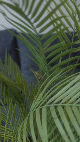 Close-up view of a person assembling an artificial plant by attaching green leaves to the stem. Hands arranging decorative foliage during a DIY home decor project indoors.