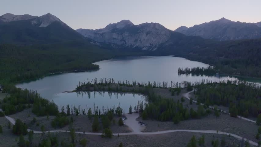 Aerial view of Redfish Lake surrounded by dense pine forests and rugged mountain peaks at dusk in Stanley, Idaho, United States.