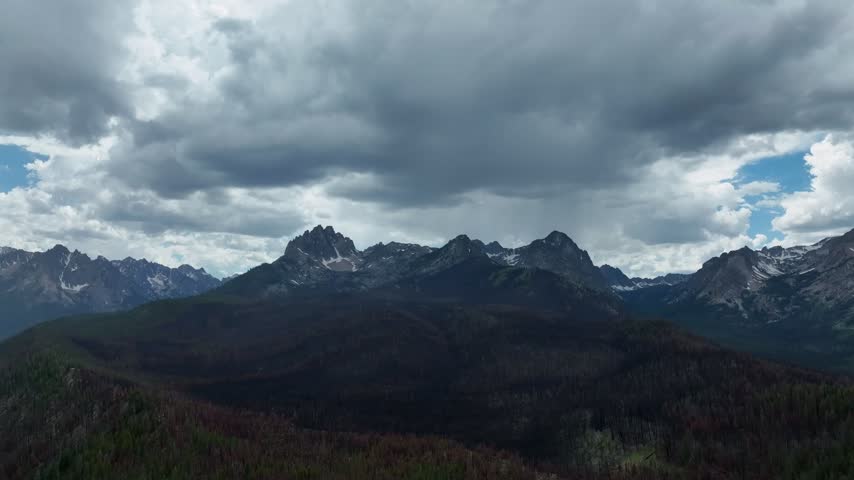 Aerial view of the rugged Sawtooth Mountains under a dramatic cloudy sky with dark storm clouds over the peaks in Stanley, Idaho, United States.