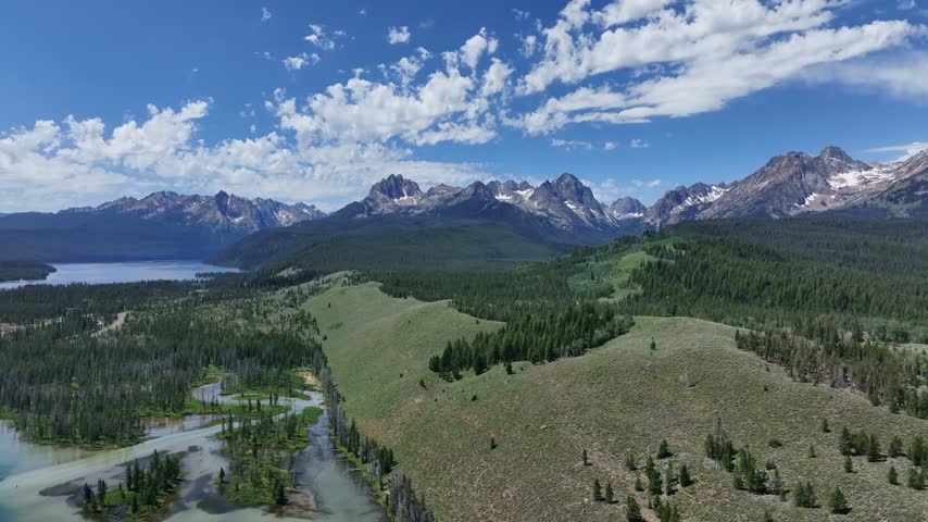 Aerial view of the jagged Sawtooth Mountains rising above the blue waters of Redfish Lake and surrounding pine forests near Stanley, Idaho, United States.
