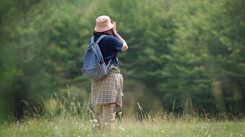 Female travel photographer taking photos with a DSLR camera while walking through a beautiful green forest, capturing nature exploration, outdoor adventure and travel photography.
