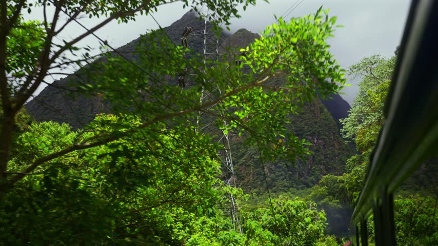 Train Machu Picchu Peru Rail Sacred Valley jungle Ollantaytambo in route Aguas Clientes Urubamba river Peru Peruvian Andes mountains range peaks Inca Trail rainy season cloudy tower pan up