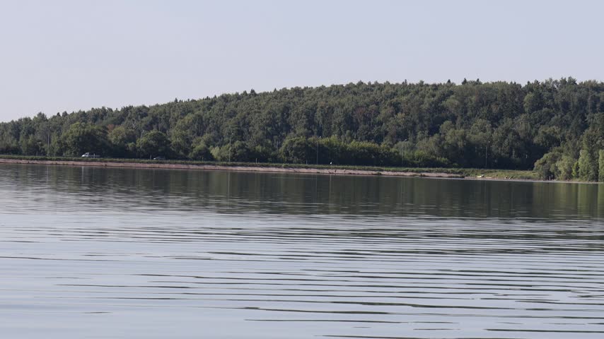 Wide shot of Lake Senezh embankment bordered by a dense forest hill