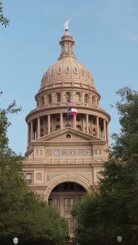 Vertical establishing shot of the historic Texas State Capitol building and distinctive dome in downtown Austin, Texas, beneath a clear blue sky. 15317  