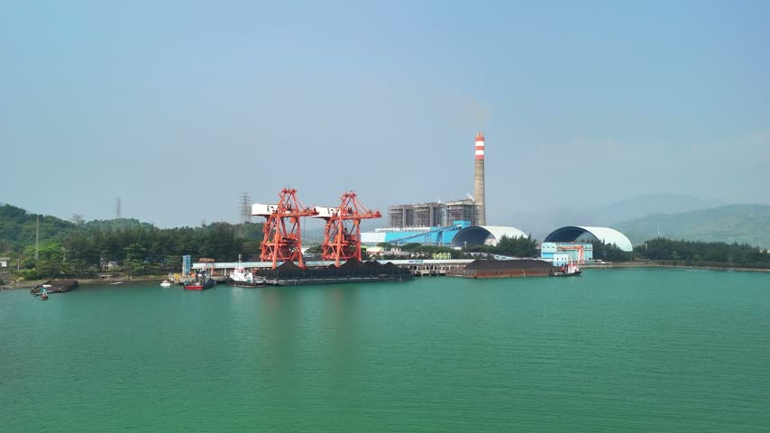 Aerial view of a coal power plant with large red cranes loading coal onto barges in a coastal bay symbolism energy production, industry, infrastructure