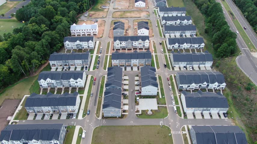 Drone forward tracking shot showing a high angle perspective of newly built multi family townhouses, residential construction site progress, and freshly paved asphalt streets in a master planned suburban community subdivision.