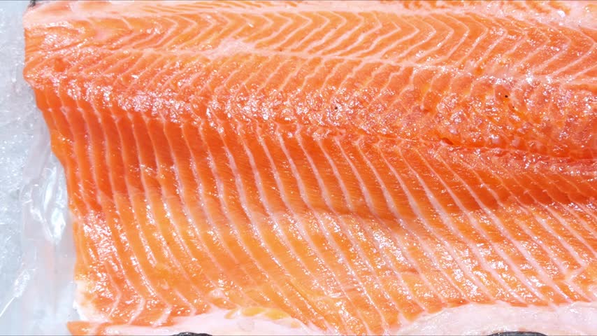 A cut of salmon with fat marbling lies in a display case.