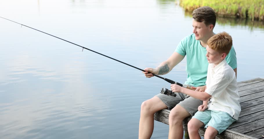 Father and his little son fishing together near river outdoors