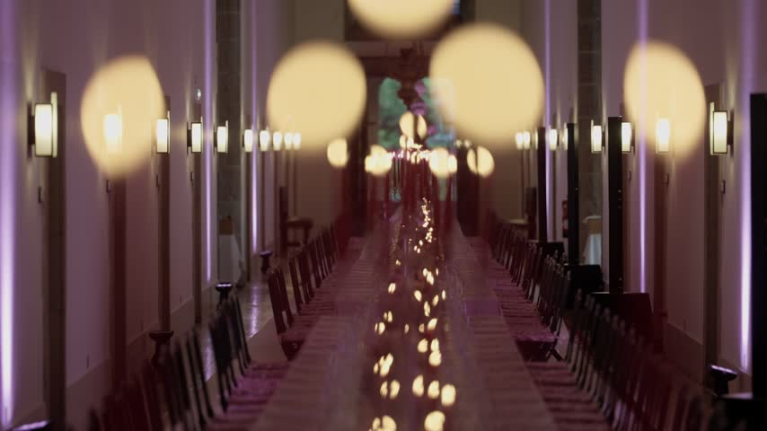 Long banquet table lined with candles and chairs in a grand hall with warm lighting