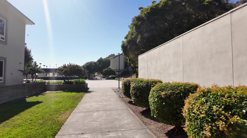 Point of view shot moving forward along a concrete path through the California State University Maritime Academy campus on a sunny day with a clear blue sky in Vallejo, California