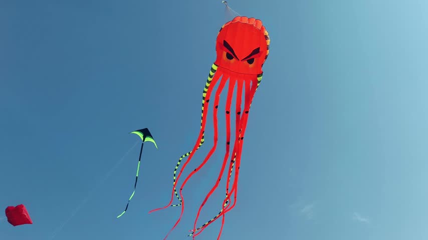 Large orange octopus kite flying high in the blue sky