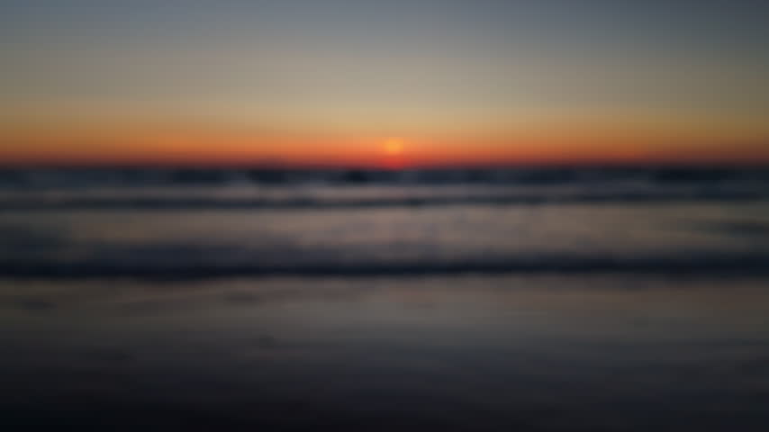Soft blurry sunset over the ocean with gentle waves and a calm beach shoreline, creating a peaceful evening background with warm colors and a dreamy mood
