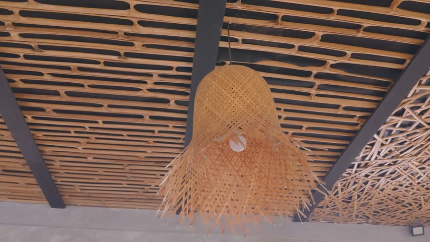 Woven bamboo lamp shade hanging from a modern decorative ceiling with wooden slats and abstract stick texture.	