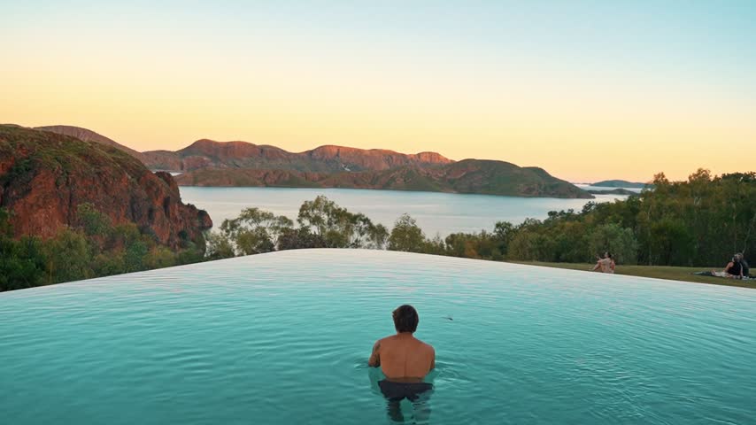 Beautiful footage of a man swimming in infinity pool during sunset with a stunning scenery.
