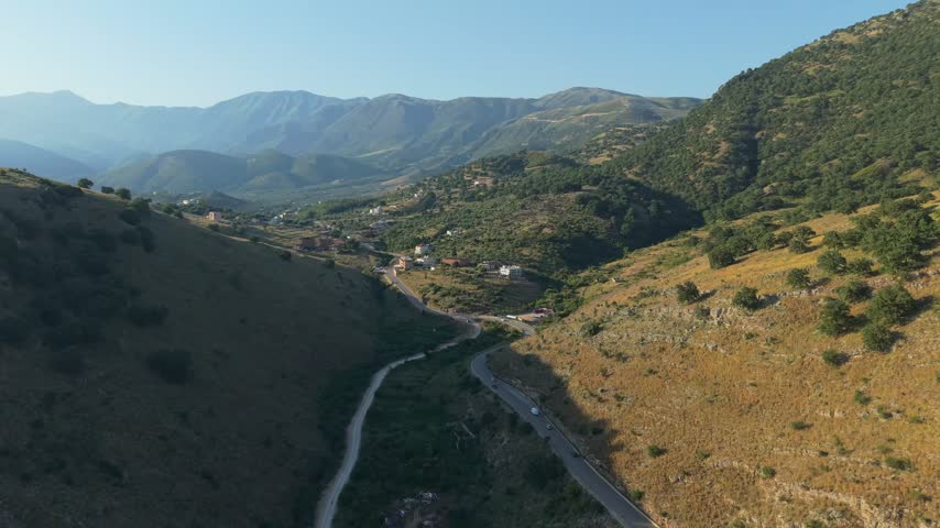 Aerial view of the winding road through the green valley surrounded by mountains near Himare, Vlore County, Albania.